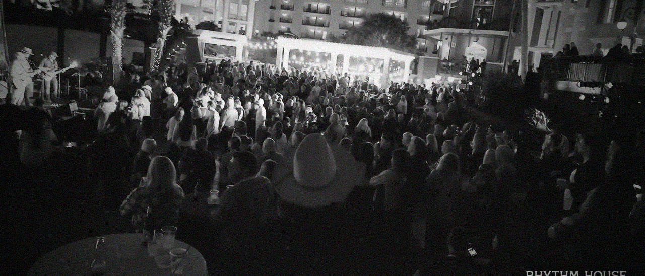 A packed courtyard crowd watching a live band at a Rhythm House night